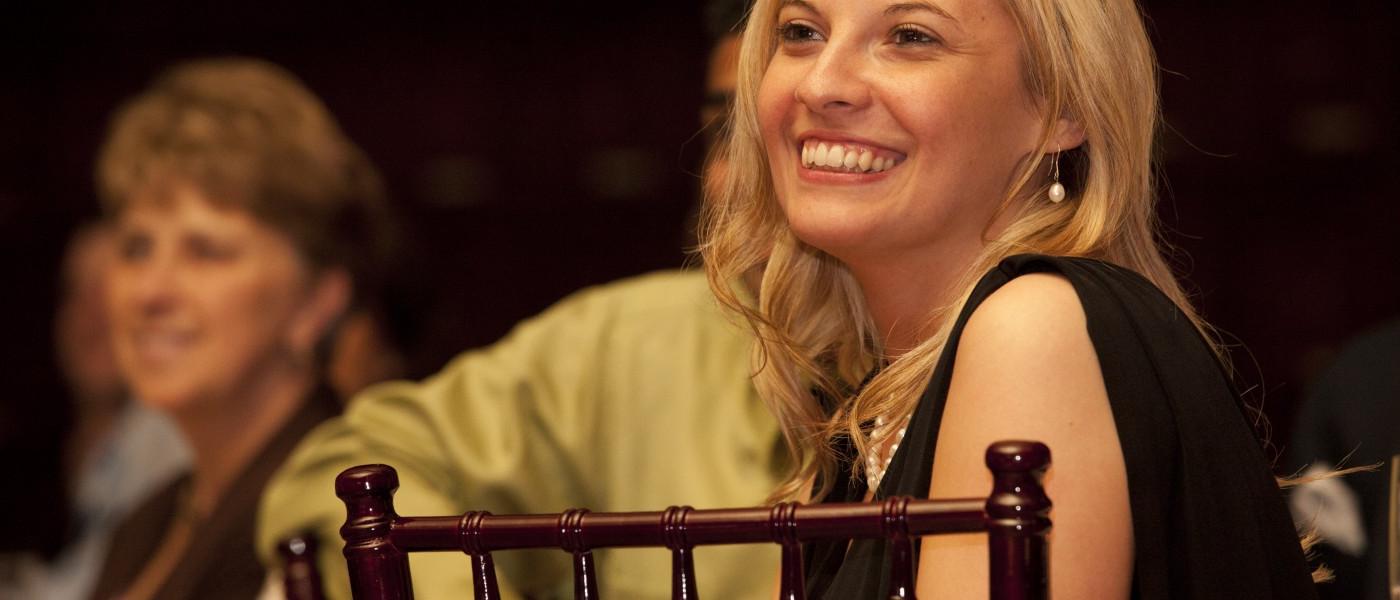 A female U N E pharmacy student sits smiling at a black tie event  